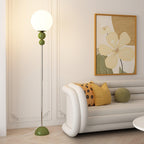 Clérachic green floor lamp lit on herringbone parquet, its chrome stem set against a panelled wall beside a cream curved sofa.