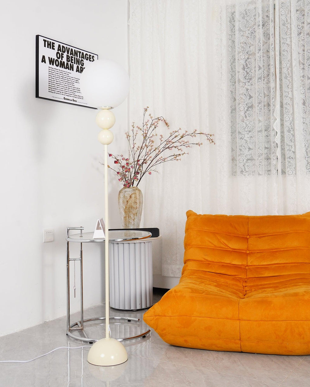 Clérachic milky white floor lamp beside a chrome-framed glass side table, its opal globe reaching the corner of a black-and-white text poster.