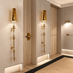 Clérachic slim gold wall lamps with a tapered shade and stacked spherical beads, lit along a pale corridor with a jute rug.