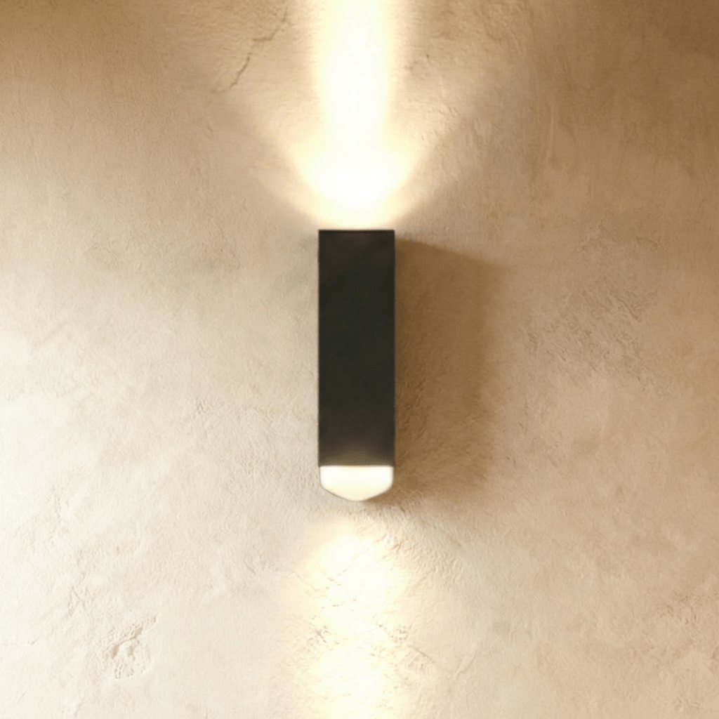 Clérachic black rectangular aluminium wall lamp casting a beam of light up and down a limewashed wall.
