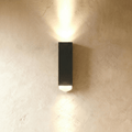 Clérachic black rectangular aluminium wall lamp casting a beam of light up and down a limewashed wall.