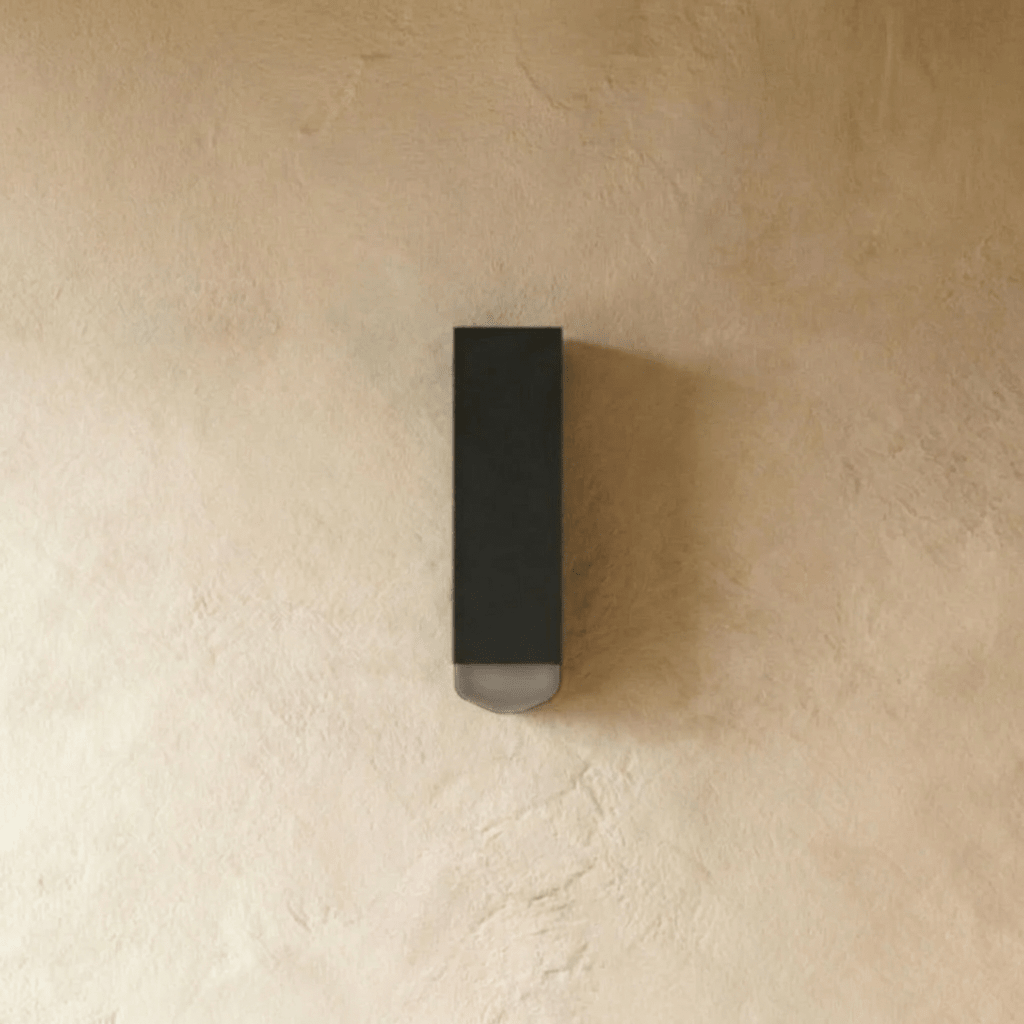 Clérachic black rectangular wall lamp unlit, with a frosted lens at its base, mounted on a plastered wall.