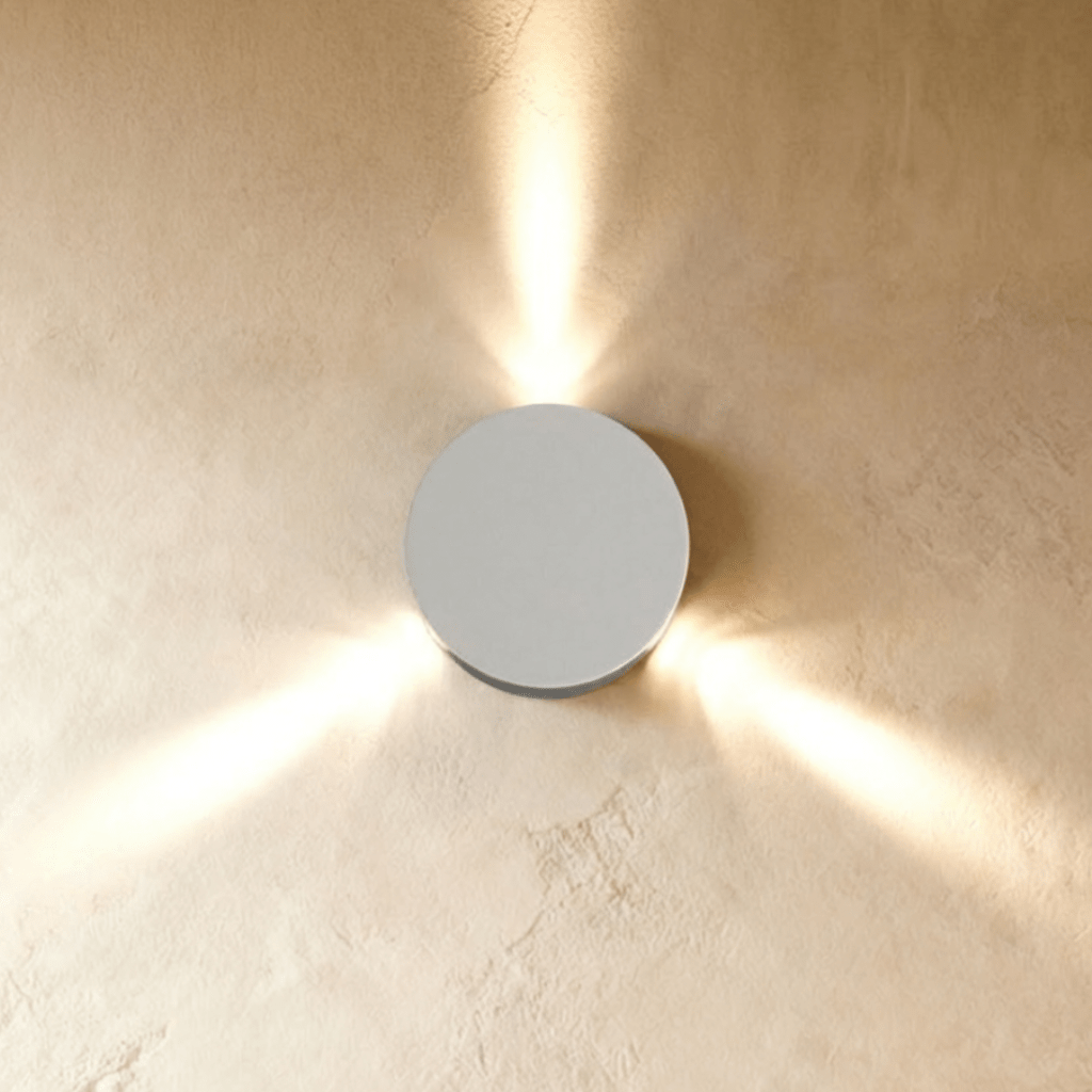 Clérachic white round wall lamp throwing three narrow beams of warm light across a plastered wall.
