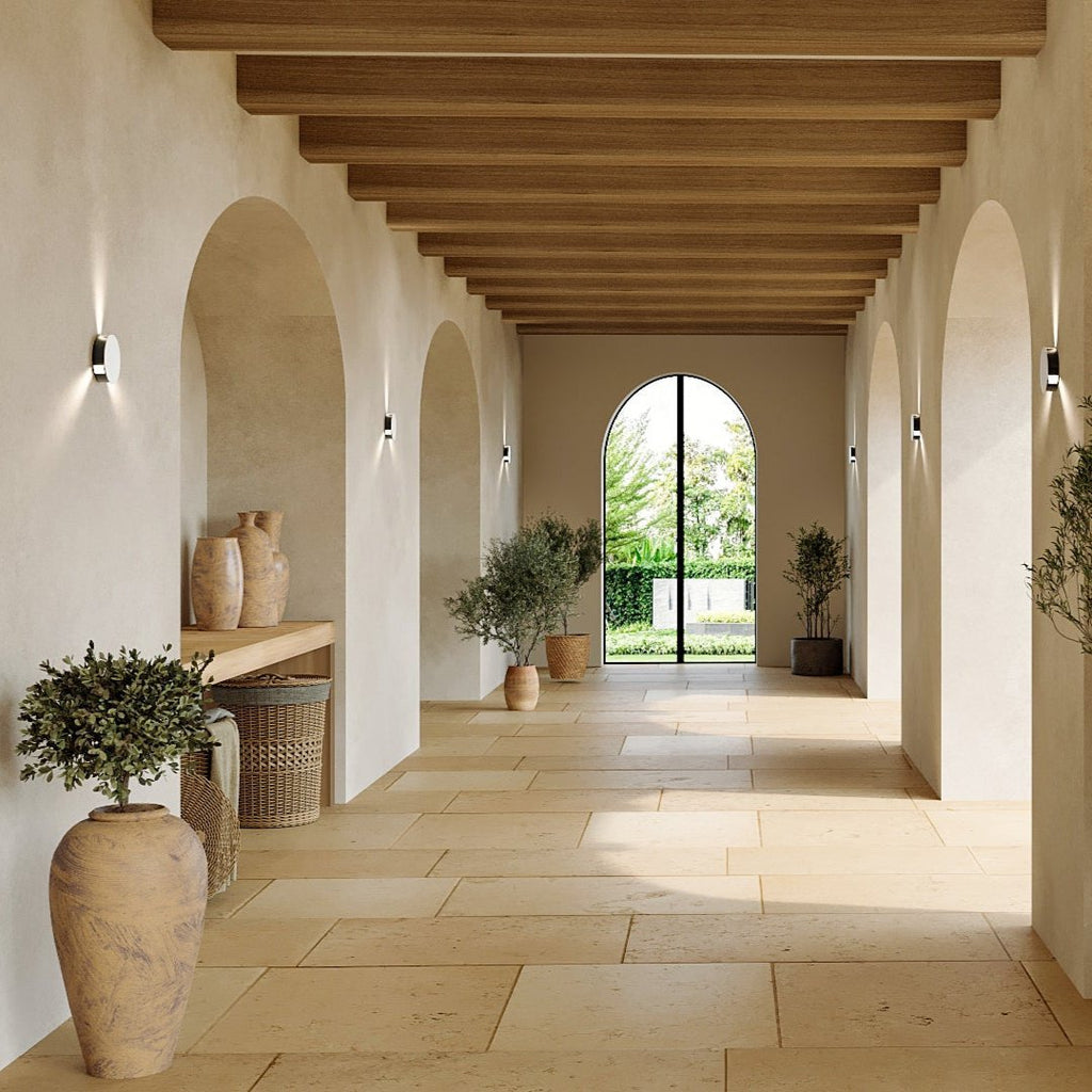 Clérachic black round wall lamps lining a pale arched stone corridor, each throwing light up and down the wall.