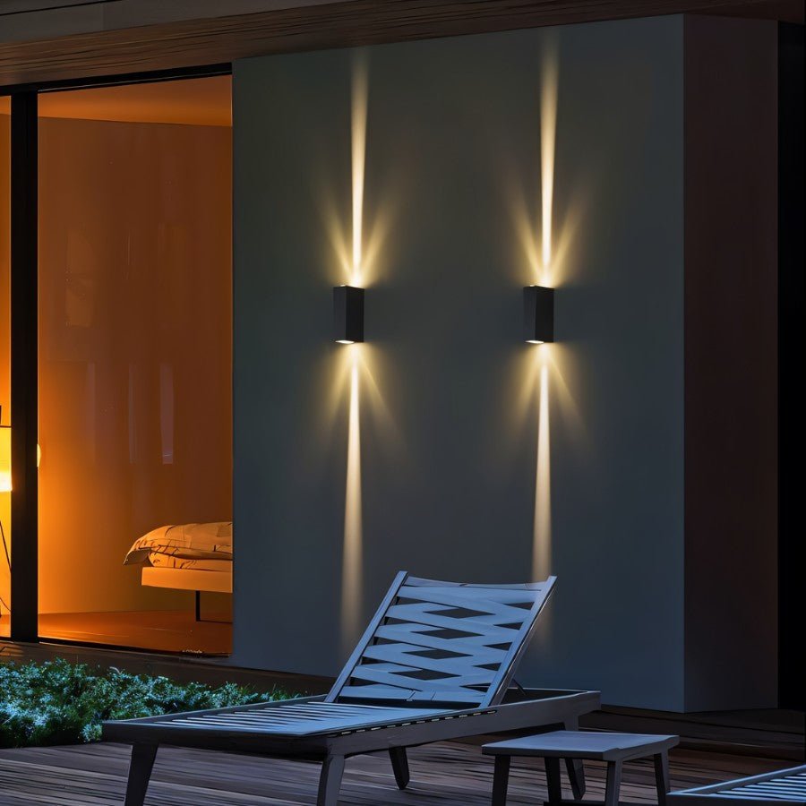 Clérachic two black rectangular wall lamps on an outdoor wall at night, beams running up and down above a lounger.