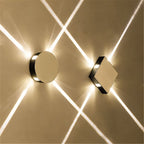 Clérachic polished metal round and square wall lamps, each shooting crossing beams of light over a warm wall.
