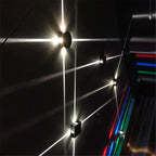 Clérachic black round and square wall lamps on a dark wall, long beams of light cutting across it beside coloured lights.