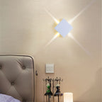 Clérachic white square wall lamp on a cream wall above a bedside, with four beams radiating from its corners.