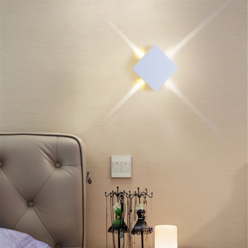 Clérachic white square wall lamp on a cream wall above a bedside, with four beams radiating from its corners.