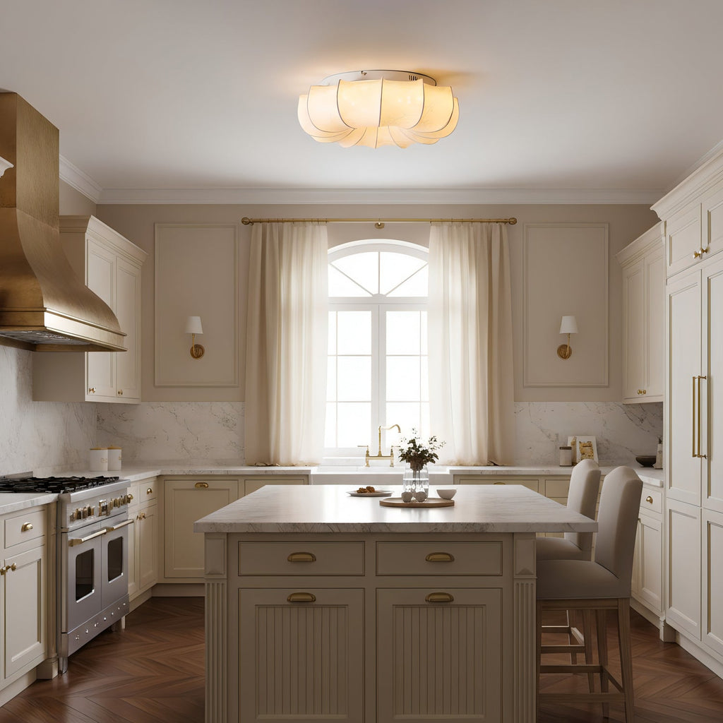 A Clérachic fabric ceiling light glowing above a cream kitchen with an island, a brass hood and an arched window.