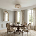 A Clérachic ceiling light, unlit, above a round dark wood dining table with floral chairs and a gilt mirror on the wall.