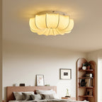 Clérachic fabric flush light lit above a bedroom with a wooden headboard, a corner shelf and neutral bedding.