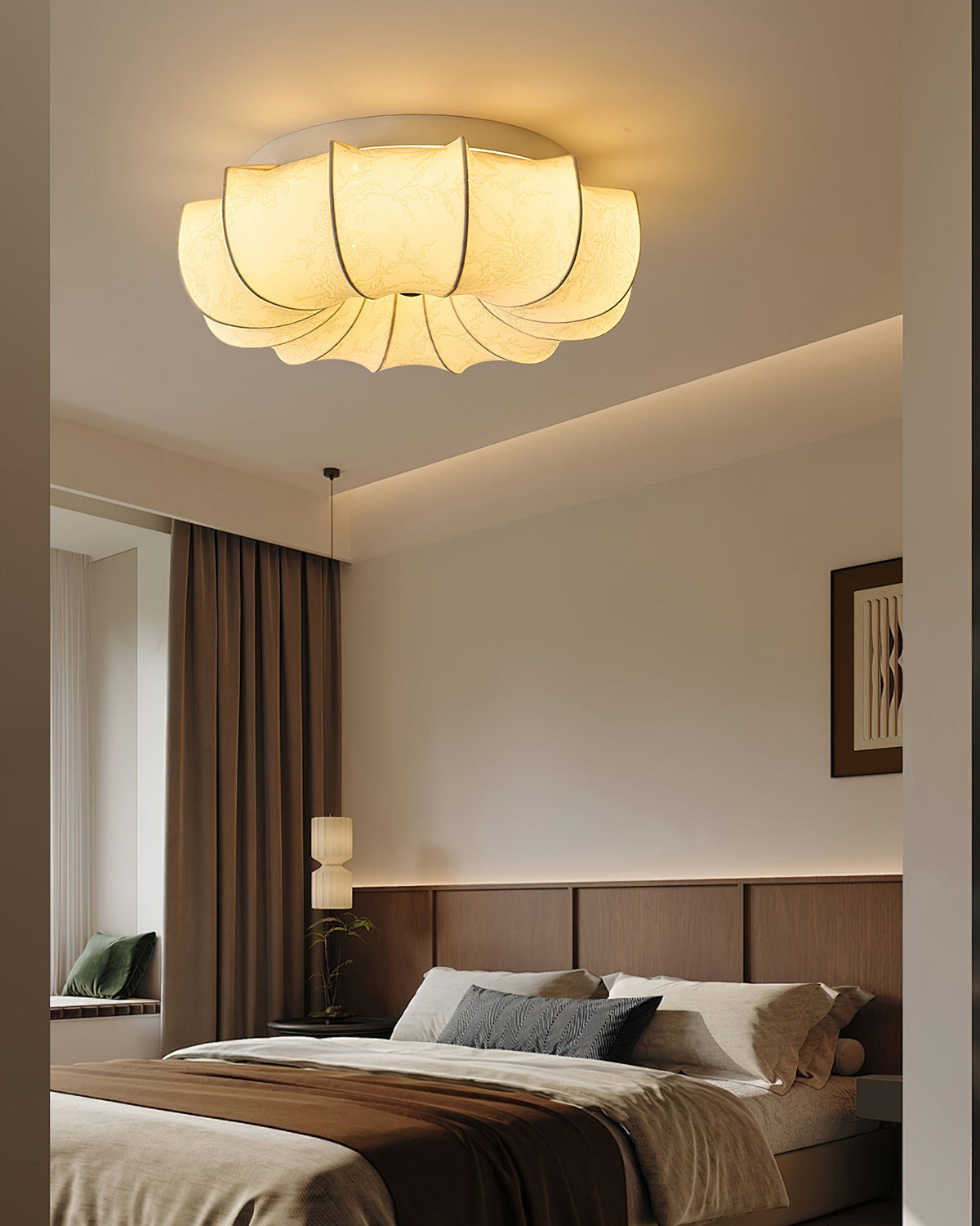 Clérachic fabric ceiling light lit above a bed with brown and grey bedding, a wood-panelled headboard wall and a framed print.