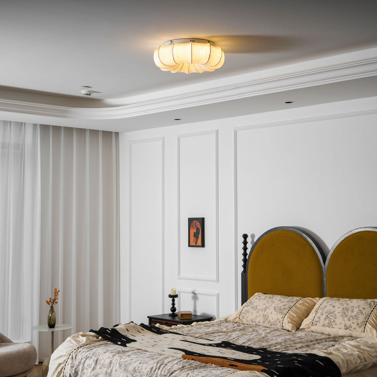 A small, lit Clérachic fabric ceiling light seen from the far side of a white panelled bedroom with a mustard headboard.