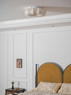 Clérachic ceiling light, unlit, in a pale cream shade above a white panelled bedroom with a mustard arched headboard.