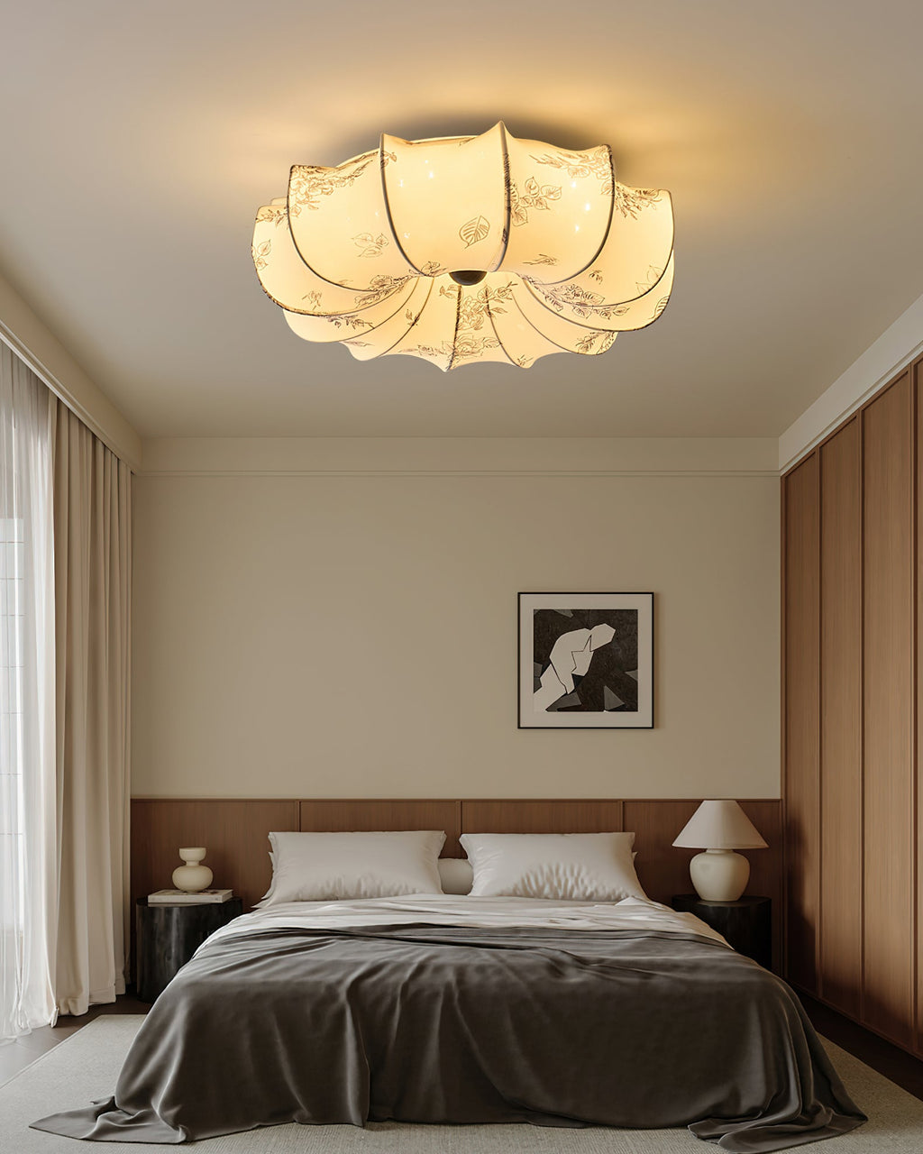 A Clérachic ceiling light glowing over a neat bed with grey bedding and a table lamp, with brown wood panelling at the side.