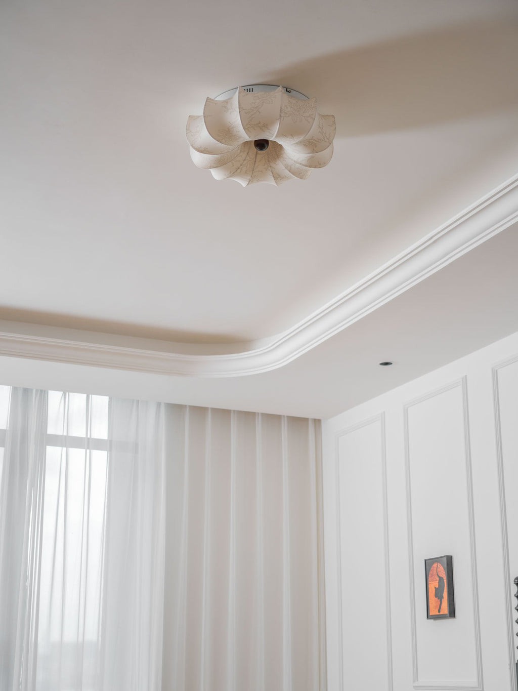 Clérachic ceiling light, unlit, seen from the corner of a white room, with the petal shape clear against the ceiling.