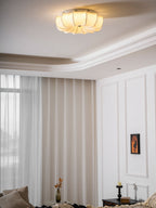 Lit Clérachic fabric ceiling light above a white panelled bedroom, with sheer curtains and a small framed print.