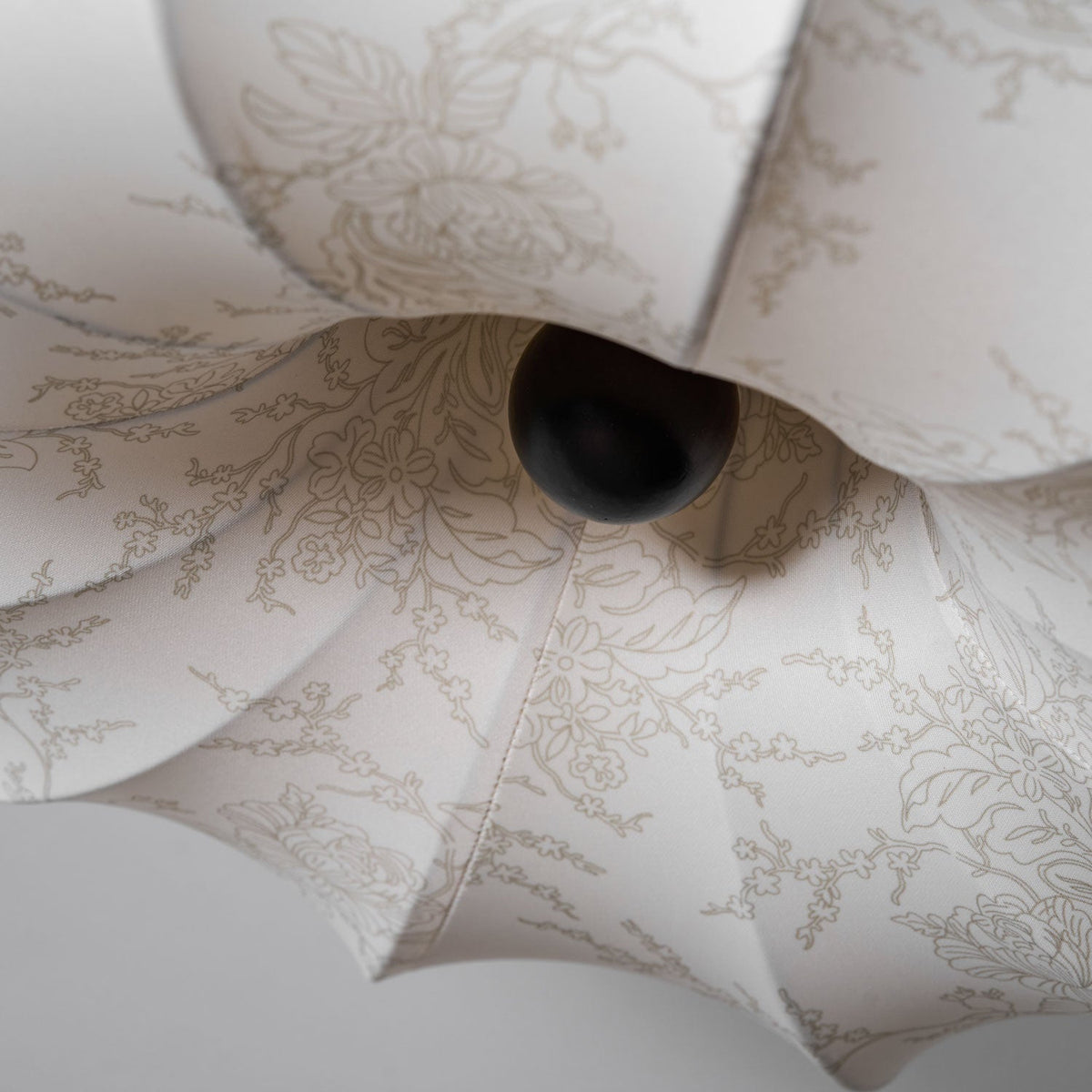 Detail of the dark round knob at the centre of this Clérachic ceiling light, surrounded by fabric petals with a fine floral print.