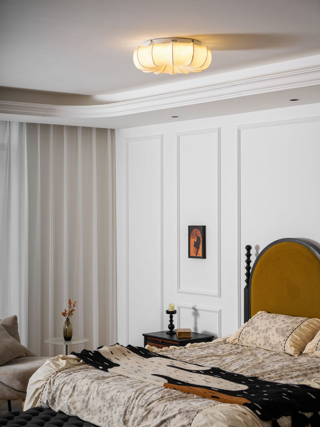 Lit Clérachic fabric ceiling light above a white panelled bedroom, with a mustard headboard and a table lamp at the side.