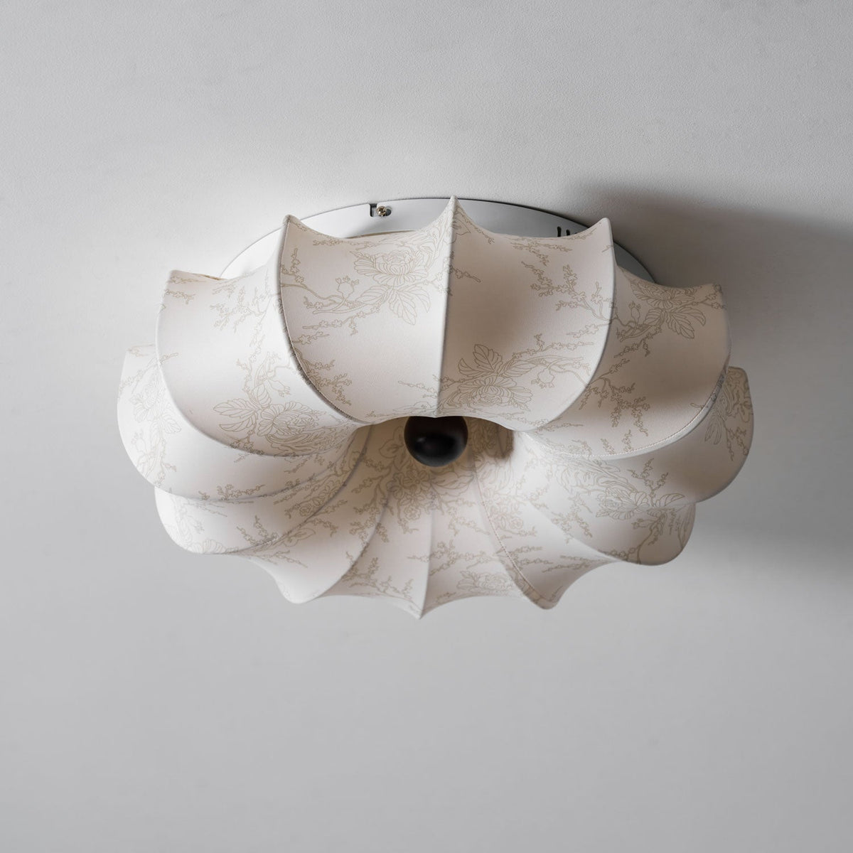 View from below of this Clérachic ceiling light, unlit, with its folded fabric petals and dark centre knob.