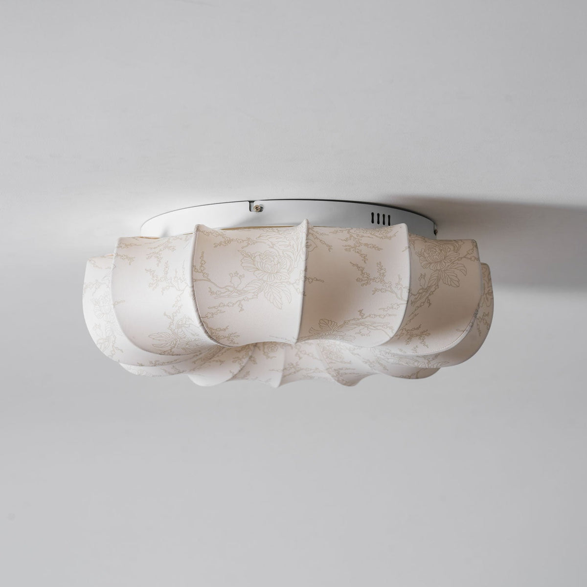 Side view of the white base plate and fabric petals on this Clérachic ceiling light, seen close to the ceiling.