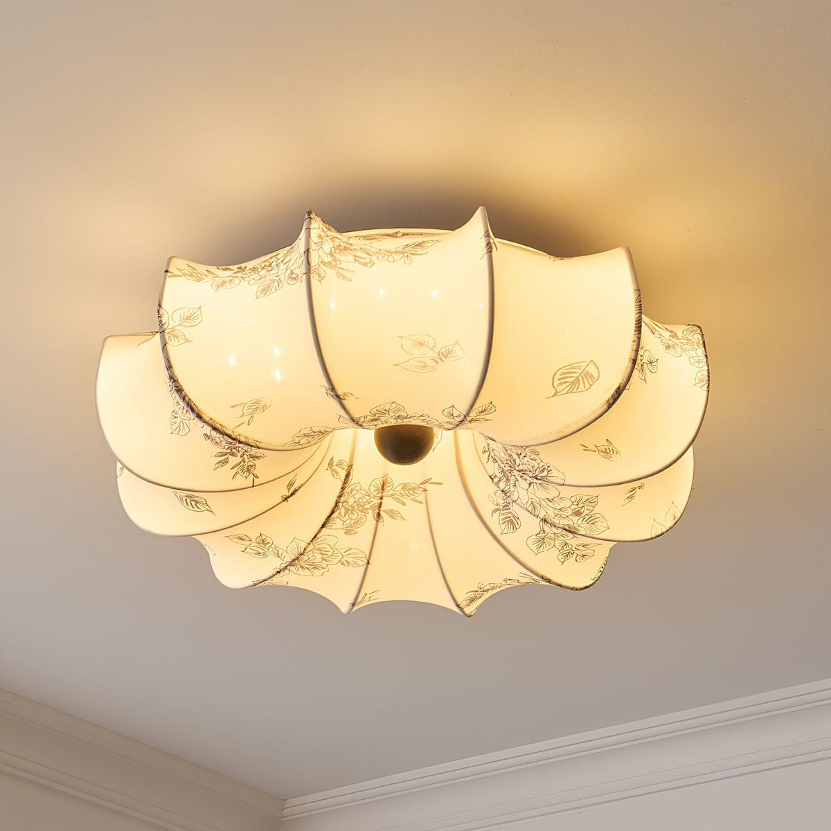 Warm-lit Clérachic fabric ceiling light with a floral print, seen from below with a pale ceiling edge at the corner.