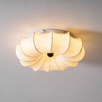 Clérachic fabric ceiling light lit warm, with a faint pattern in the fabric and a white base plate against a pale ceiling.