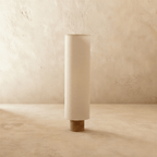 Clérachic floor lamp switched off, a tall beige fabric cylinder shade with hand-laced edges on a round wooden base.