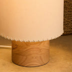 Close view of the Clérachic floor lamp base, a round light-wood cylinder under the laced beige shade, with a white cord.