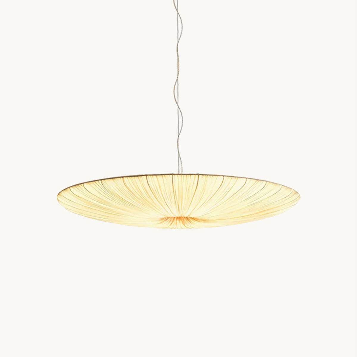 A shallow, gathered beige fabric disc hangs from a thin twisted cord, this Clérachic pendant light glowing on a plain white backdrop.