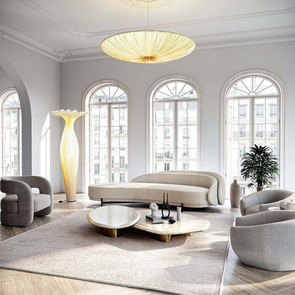 Lit Clérachic pendant light hanging in a tall room with arched windows, a curved cream sofa and a pale rug below.