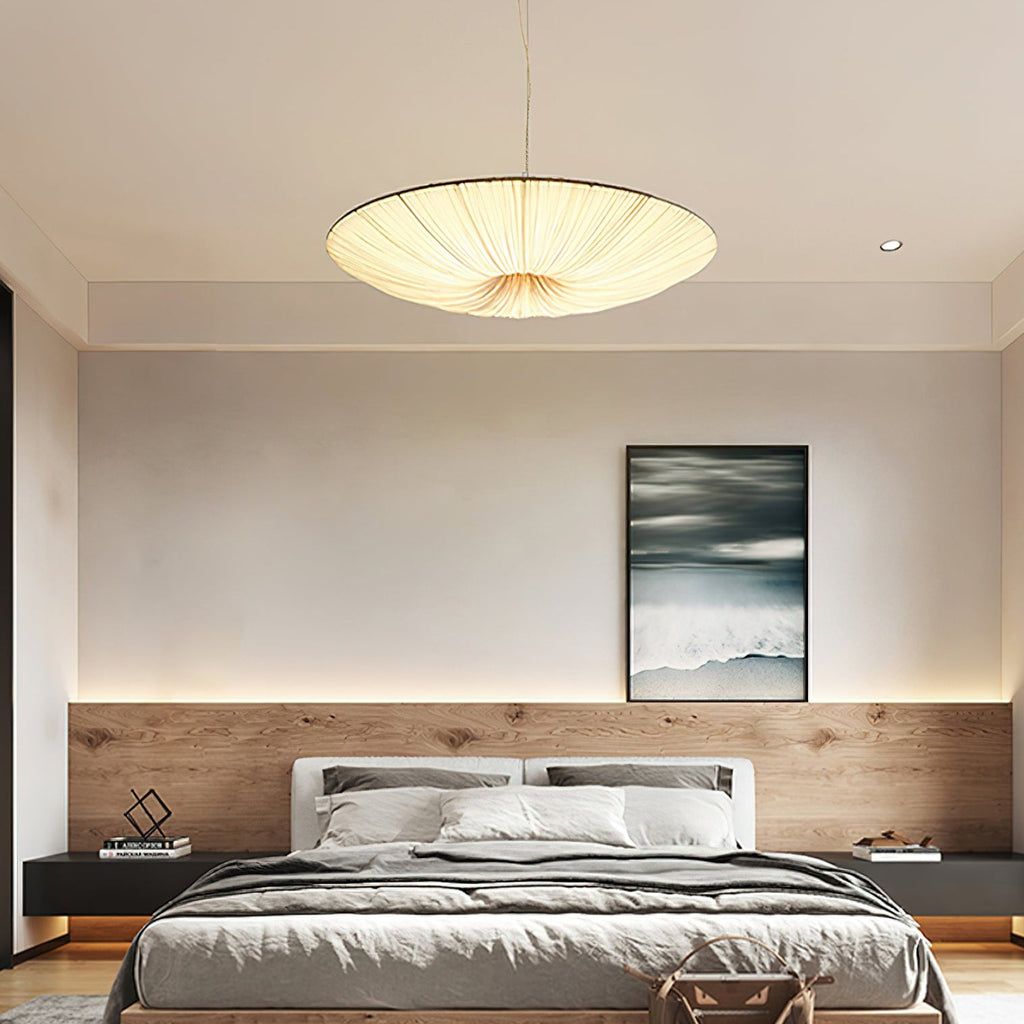 Above a low bed with a wood-panelled headboard wall, a glowing Clérachic fabric pendant hangs in a calm grey bedroom.