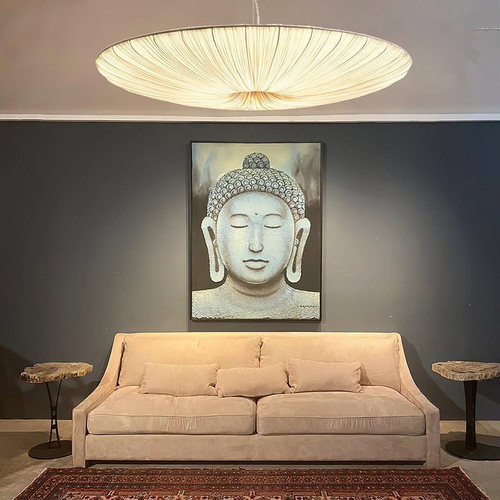 The ribbed underside of this Clérachic pendant glows above a peach sofa and a large stone-grey Buddha portrait on a dark wall.