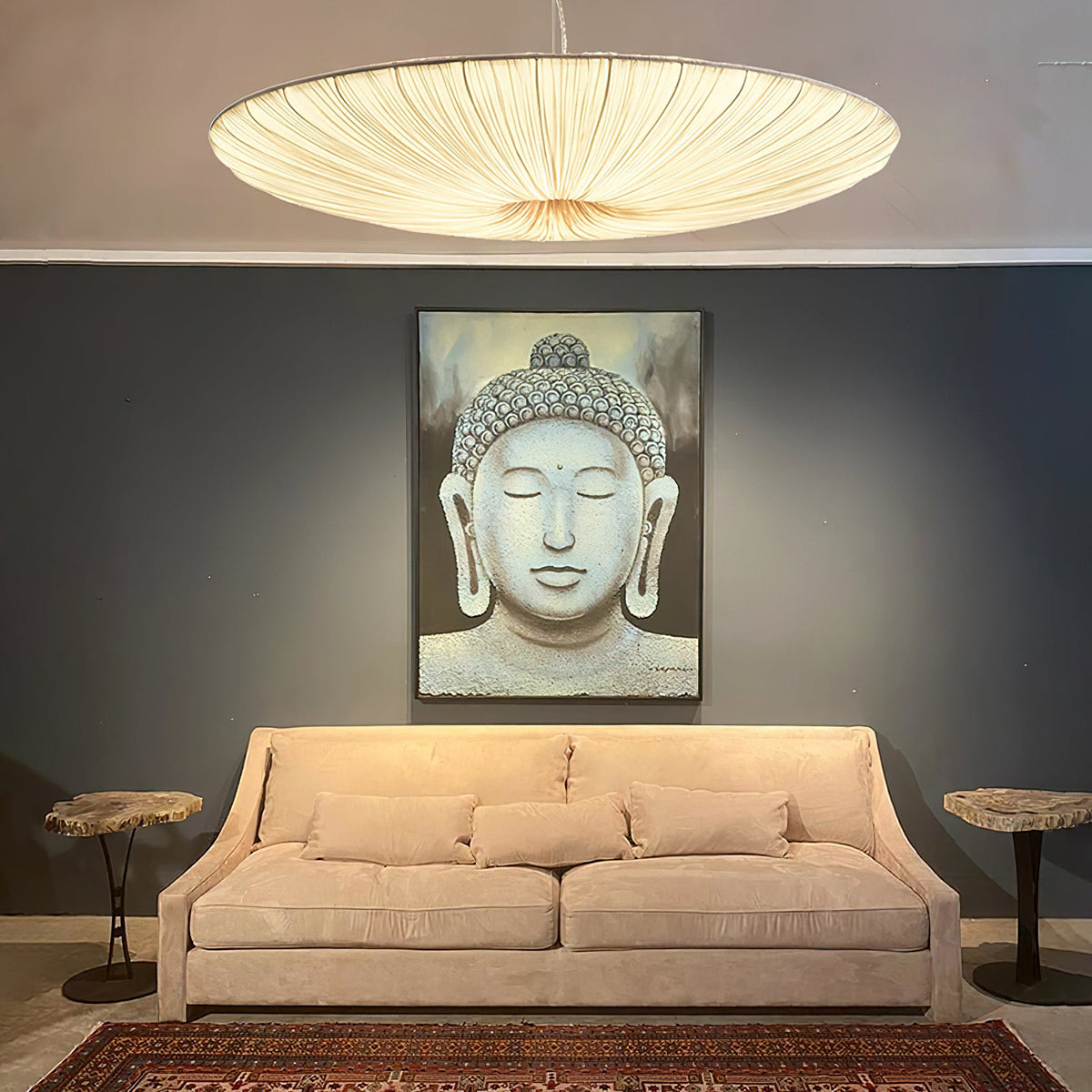 The ribbed underside of this Clérachic pendant glows above a peach sofa and a large stone-grey Buddha portrait on a dark wall.