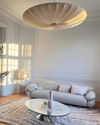 A greyish-beige version of this Clérachic pendant hangs low in a pale panelled room, over a grey sofa and a glass coffee table.