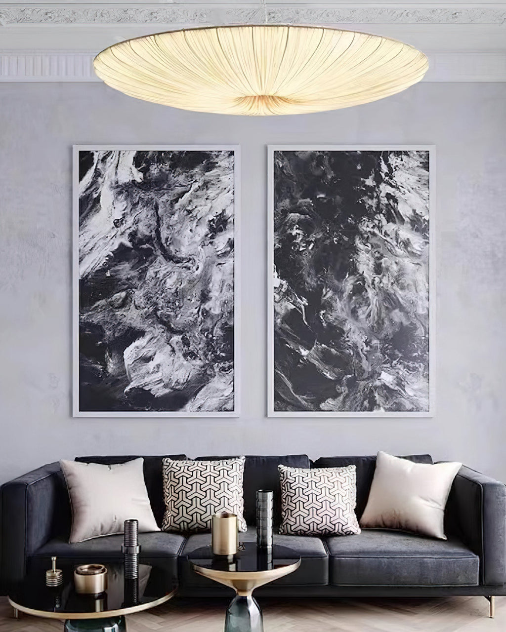 A glowing Clérachic pendant hangs above a dark sofa, with two black-and-white abstract prints on the grey wall behind.