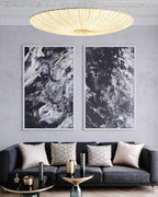 A glowing Clérachic pendant hangs above a dark sofa, with two black-and-white abstract prints on the grey wall behind.