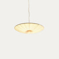 A shallow beige Clérachic fabric pendant lit warm, with its gathered folds meeting at the centre, against a soft grey backdrop.