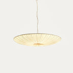 A wider, flatter Clérachic pendant with a beige fabric shade and gathered folds, hanging from a thin cord on a light backdrop.