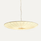 A broad beige fabric shade with fine gathered pleats, this Clérachic pendant hanging from a twisted cord on a light grey backdrop.