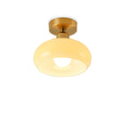 Lit beige glass dome on a short brass stem and round canopy, a Clérachic ceiling light on a white background.