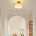 A Clérachic flush-mount ceiling light glowing in a pale hallway, with an arched doorway and a small shelf beyond.