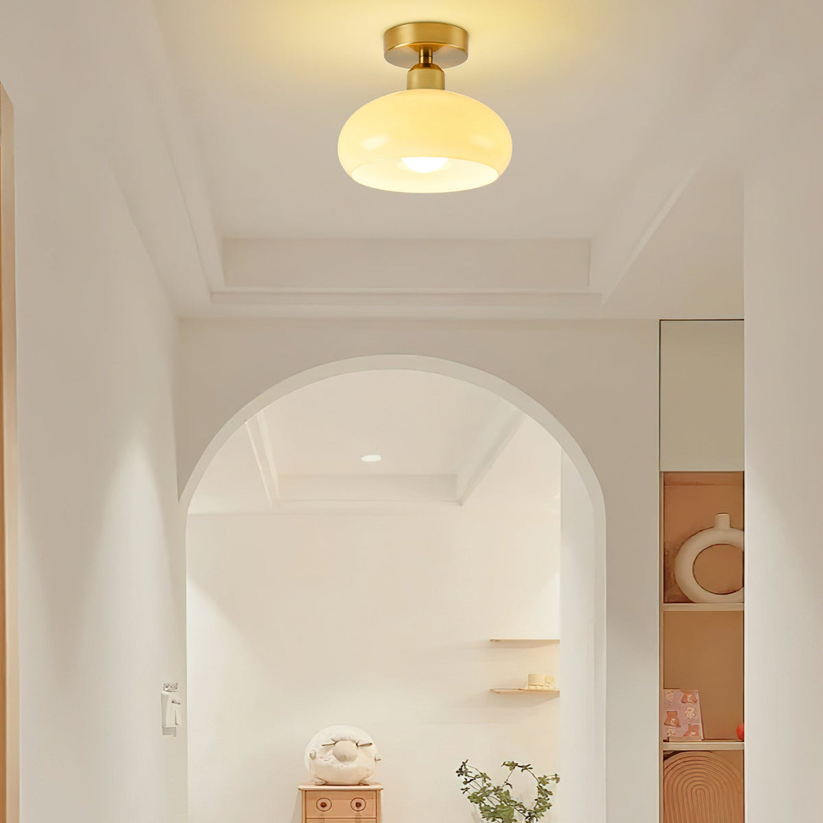 A Clérachic flush-mount ceiling light glowing in a pale hallway, with an arched doorway and a small shelf beyond.