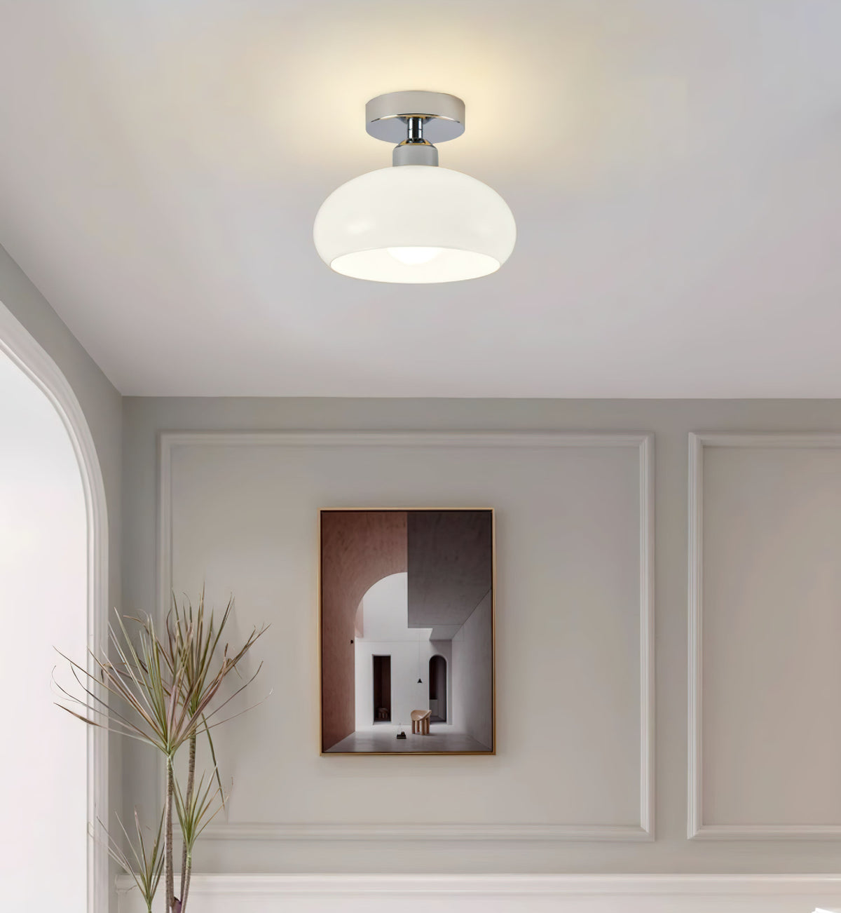 This Clérachic ceiling light in white glass with a chrome canopy, above a grey panelled wall with a framed print and dried stems.