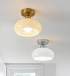 A beige glass Clérachic ceiling light with a brass canopy above a white glass one with a chrome canopy, shown side by side.
