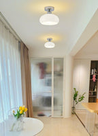 Two white glass Clérachic ceiling lights along a bright corridor with sheer curtains and a frosted glass door.