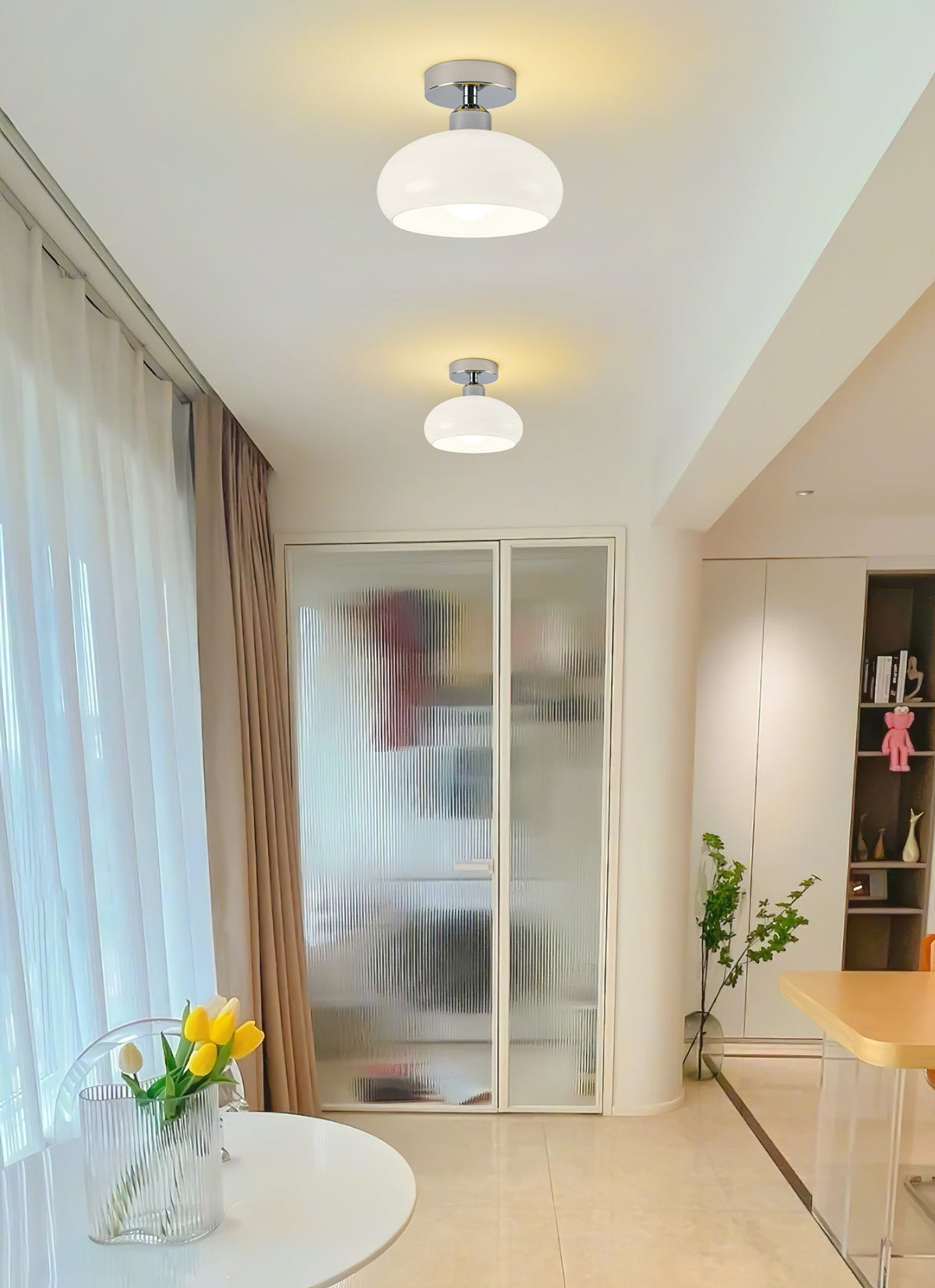 Two white glass Clérachic ceiling lights along a bright corridor with sheer curtains and a frosted glass door.