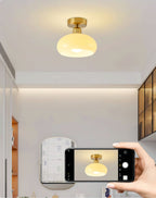 A Clérachic ceiling light lit above a room with a mirror and glass-fronted cabinets, with a phone photographing it.