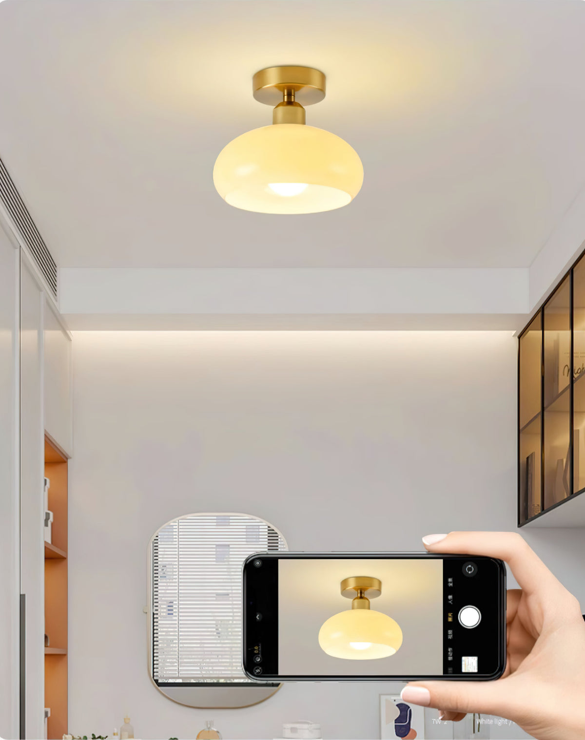 A Clérachic ceiling light lit above a room with a mirror and glass-fronted cabinets, with a phone photographing it.